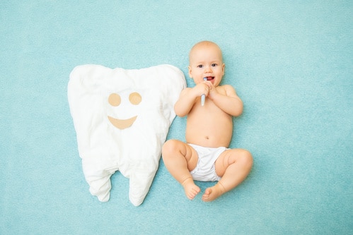 Cute Baby Lies With A Toothbrush On A Blue Background. White Tooth Made Of Fabric. Medicine, Dentistry, Health Concept